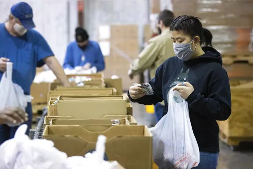 Volunteer Ana Willis fills a bag with food items for the backpack program at Feeding America food bank in Elizabethtown, Ky., Monday, Jan. 17, 2022. Food banks across the country are experiencing a critical shortage of volunteers as the omicron variant frightens people away from group activities. (AP Photo/Michael Clubb)