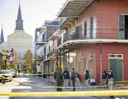 Members of the FBI work on Orleans Street and Bourbon Street by St. Louis Cathedral in the French Quarter near where a suspicious package was detonated during the investigation of a truck crashing into pedestrians on Bourbon Street Wednesday, Jan. 1, 2025. The suspect was also seen leaving the rolling cooler by the corner of the red building which contained the package that was previously detonated. (AP Photo/Matthew Hinton)
