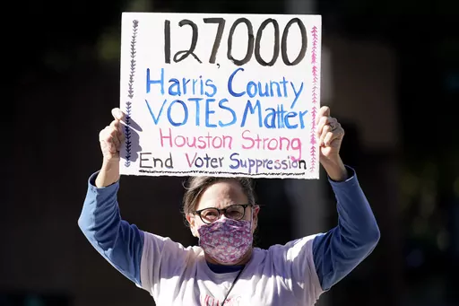 Demonstrator Gina Dusterhoft holds up a sign as she walks to join others standing across the street from the federal courthouse in Houston, Monday, Nov. 2, 2020, before a hearing in federal court involving drive-thru ballots cast in Harris County. (AP Photo/David J. Phillip, File)