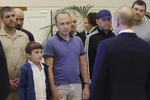 A man identified as Pablo González, a freelance journalist from Spain who had been based in Poland since 2019, second from left with shaved head, listens to Russian President Vladimir Putin, back to a camera, speaking to released Russian prisoners, part of the biggest prisoner swap between the United States and Russia in post-Soviet history, upon their arrival at the Vnukovo government airport outside Moscow, Russia, on Thursday, Aug. 1, 2024. Gonzalez had another passport and another name: Pav