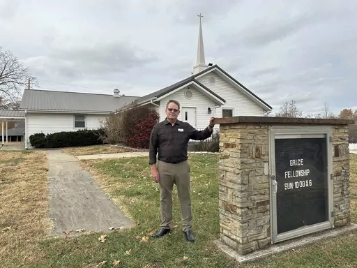 Pastor Kenny Batson stands near a sign displaying the worship service times of Grace Fellowship Church on Nov. 16, 2023, in El Dorado Springs, Mo. Batson was convicted of a series of crimes in the 1990s but became a Christian pastor after being released from prison. He was pardoned by Missouri Gov. Mike Parson. (AP Photo/David A.Lieb)