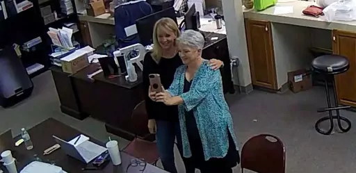 In this Jan. 7, 2021, image taken from Coffee County, Ga., security video, Cathy Latham, right, appears to take a selfie with a member of a computer forensics team inside the local elections office. Lawyers for three Georgia Republicans, including Latham, who falsely claimed that Donald Trump won the state and they were “duly elected and qualified” electors, are set to argue that their criminal charges should be moved from state to federal court(Coffee County, Georgia via AP)