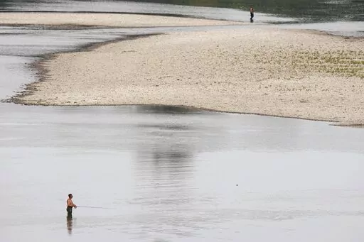 People fish near a hydroelectric power plant at Isola Serafini, on the Po river in San Nazzaro, Italy, Wednesday, June 15, 2022. The drying up of the river is jeopardizing drinking water in Italy's densely populated and highly industrialized districts and threatening irrigation in the most intensively farmed part of the country.  (AP Photo/Luca Bruno)