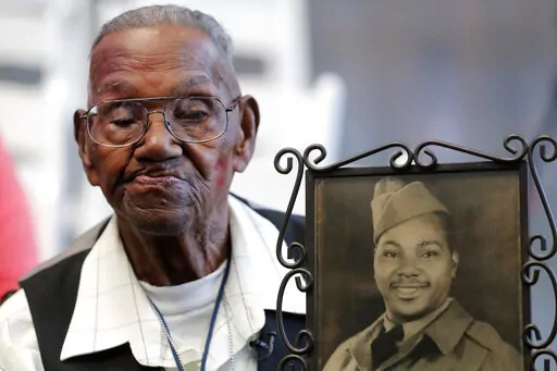 World War II veteran Lawrence Brooks holds a photo of him taken in 1943, as he celebrates his 110th birthday at the National World War II Museum in New Orleans, on Sept. 12, 2019.  Brooks, the oldest World War II veteran in the U.S. — and believed to be the oldest man in the country — died on Wednesday, Jan. 5, ,2022 at the age of 112.  (AP Photo/Gerald Herbert, File)