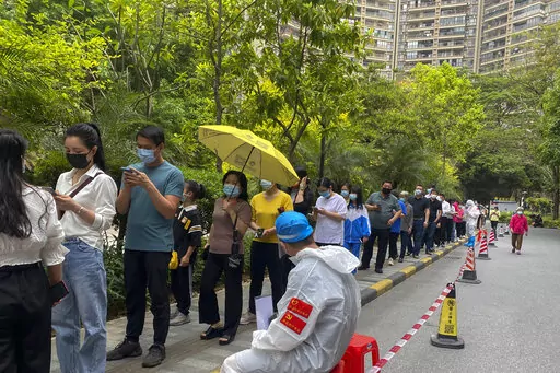 Workers in protective gear watch over residents line up for the COVID-19 test at a residential block, Monday, April 11, 2022, in Guangzhou in south China's Guangdong province. The manufacturing hub of Guangzhou began tightly restricting departures and arrivals Monday as eastern China battles the country's latest major COVID outbreak. (Chinatopix Via AP)
