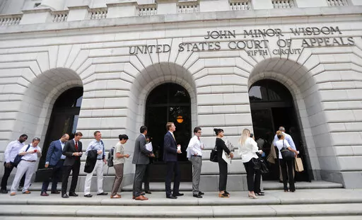 In this Tuesday, July 9, 2019 file photo, People wait in line to enter the 5th Circuit Court of Appeals to sit in overflow rooms to hear arguments in New Orleans.  President Joe Biden's requirement that all federal employees be vaccinated against COVID-19 is awaiting judgment from a federal appeals court after arguments in New Orleans. An administration attorney told the court Tuesday, March 8, 2022, that a federal judge in Texas overstepped his authority when he blocked the mandate.   (AP Photo