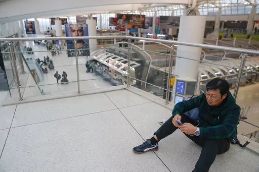 A man checks his phone in a mostly empty Terminal 1 at John F. Kennedy International Airport in New York, Friday, Feb. 17, 2023. A power outage in the terminal has stretched into a second day. The outage has stranded passengers and forced flights to be canceled or diverted to other airports. (AP Photo/Seth Wenig)