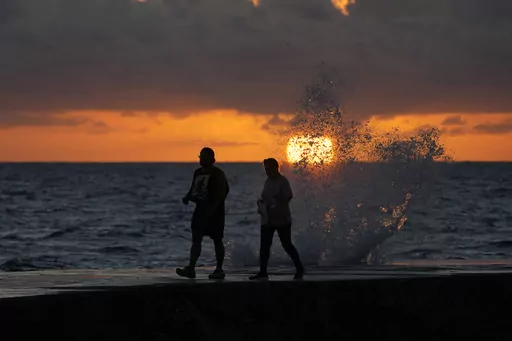 The sun rises above the Atlantic Ocean as waves crash near beach goers walking along a jetty, Dec. 7, 2022, in Bal Harbour, Fla. The world's oceans have suddenly spiked much hotter and well above record levels, with scientists trying to figure out what it means and whether it forecasts a surge in atmospheric warming. (AP Photo/Wilfredo Lee, File)