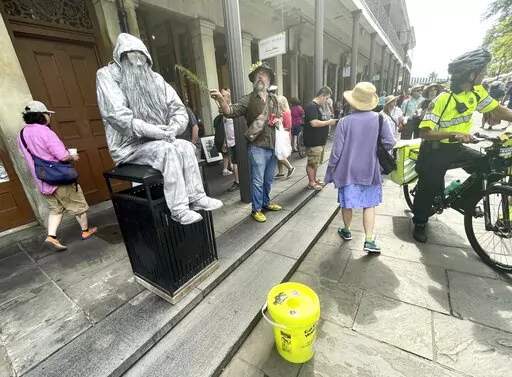 Street performer Robyn Barrett, right, stands with his business partner Jimmy Thibodaux, an imitation mime, near Jackson Square in New Orleans. Tourists pose for pictures with the scruffy, gnome-like, metallic personage with the hoodie, sunglasses and ZZ Top beard.  (Doug MacCash/The Advocate via AP)