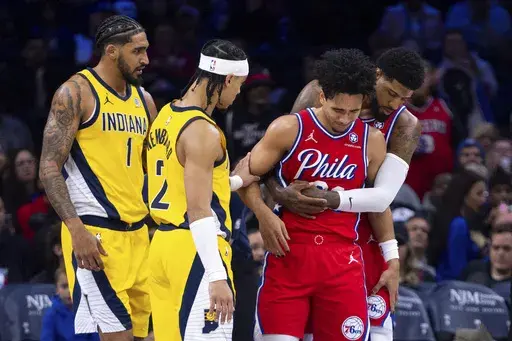 Philadelphia 76ers' Jared McCain, center right, gets helped by Paul George, right, and Indiana Pacers' Andrew Nembhard, center left, after a hard fall to the court during the first half of an NBA basketball game, Friday, Dec. 13, 2024, in Philadelphia. (AP Photo/Chris Szagola)