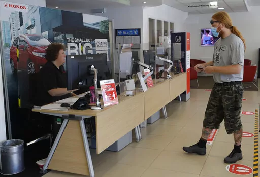 A customer wearing a face mask to protect against coronavirus, social distances in the car servicing department at the Trident Honda car dealership in Ottershaw, England, Friday, May 29, 2020. A new car warranty is a contract between the automaker and the vehicle owner. But if the owner doesn’t hold up his or her part of the bargain, it could void all the coverage. Here are a few reasons why your warranty claim can be denied and tips on how to avoid any issues down the road.  (AP Photo/Kirsty 