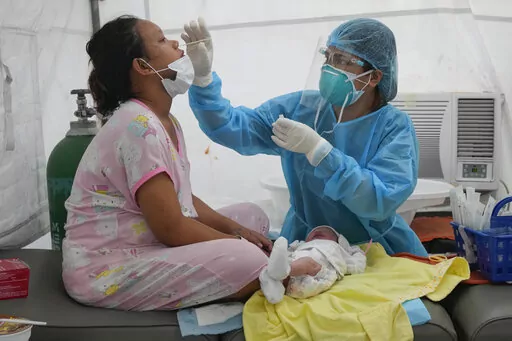 Medical Technologist Erika Alvarado performs a COVID-19 test on a patient who just delivered a baby outside a hospital in Manila, Philippines on Friday, Dec. 24, 2021. In the Philippines, one of the worst-hit by the pandemic in Southeast Asia, daily COVID-19 infections have considerably dropped from an average 22,000 cases just three months ago during an alarming spike set off by the delta variant to just a few hundred in recent days after a delayed vaccination campaign considerably intensified 