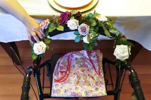 A woman holds onto the walker once belonging to her mother who died of COVID-19 while at a nursing home, as her family prays before Thanksgiving dinner, Nov. 26, 2020, in Deer Park, N.Y. A sobering study out Wednesday, April 6, 2022, from the National Academies of Sciences, Engineering, and Medicine is calling for wholesale changes in the U.S. long-term care system in the wake of more than 150,000 resident COVID-19 deaths. (AP Photo/John Minchillo, File)