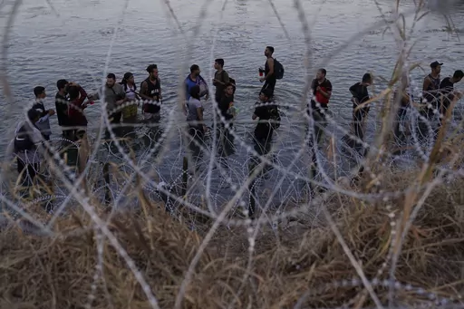 Migrants wait to climb over concertina wire after they crossed the Rio Grande and entered the U.S. from Mexico, Sept. 23, 2023, in Eagle Pass, Texas. A divided Supreme Court on Tuesday, March 19, 2024, lifted a stay on a Texas law that gives police broad powers to arrest migrants suspected of crossing the border illegally, while a legal battle over immigration authority plays out. (AP Photo/Eric Gay, File)